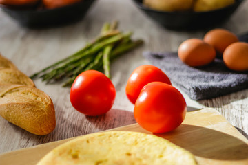Potato omelette as a typical Spanish dish along with different healthy and vegetarian ingredients such as tomatoes, onions, eggs or asparagus, accompanied by a handmade loaf of bread, selective focus