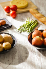 Potato omelette as a typical Spanish dish along with different healthy and vegetarian ingredients such as tomatoes, onions, eggs or asparagus, accompanied by a handmade loaf of bread, selective focus