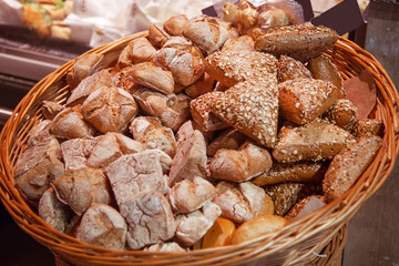 A large assortment of baked bread lies in a wooden basket.