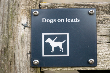 Dogs on leads black sign with symbol and text written in white.