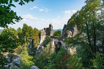 Papier peint Le pont de la Bastei Bad Schandau in Bohemian Switzerland. Bastei bridge and mountain view. Narrow rock, natural sandstone arch in Europe..Hill scenery with greenery, blue sky and sunlight.