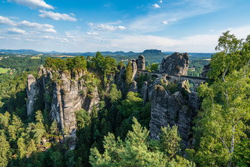 Obraz premium Bad Schandau in Bohemian Switzerland. Bastei bridge and mountain view. Narrow rock, natural sandstone arch in Europe..Hill scenery with greenery, blue sky and sunlight.