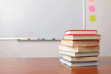 PIle of books on school desk in front of marker whiteboard in classroom. Concept of education