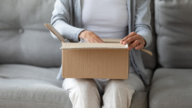 Close Up Of Young Woman Open Cardboard Box Order Shopping Online In Internet, Female Client Or Customer Sit On Sofa Unwrap Unpack Delivery Parcel Buying Things On Web, Good Delivery Concept