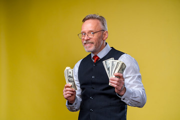 Happy exited man in glasses and white shirt holding bunch of money, looking at camera, isolated over yellow background