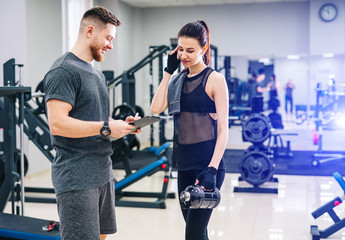 Beautiful young woman with her personal trainer at the gym discuss her progress on a clipboard held by the man. Healthy lifestyle