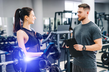 Personal handsome fitness trainer and beautiful female client in gym making workout schedule or program. Healthy life concept.