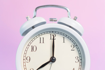 White analog classic alarm clock with black arrows on a pink creative background