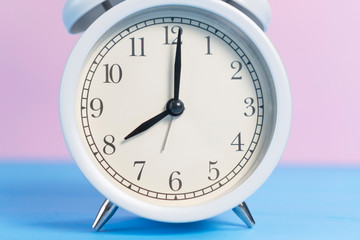 White analog classic alarm clock with black arrows on a pink and light blue creative background