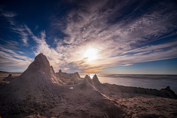 Sand castle on beach on sunset. A sandcastle on a sandy coast, blue sky. House with high towers on...
