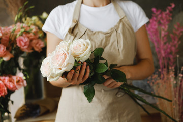 woman florist standing with bouquet of   pink roses indoor in flower shop.  Small business, workplace concept