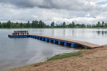 Wooden bridge for swimming on the shore of a lake. Blue sky and water, green trees, summer nature landscape.  Environmental concept, Latvia, Europe.