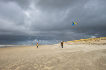 Obraz premium Young girl and boy with a colorful kite on a deserted winter beach