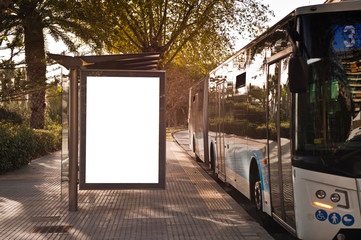 White blank vertical billboard at the bus stop on the city street. In the background of buses and...