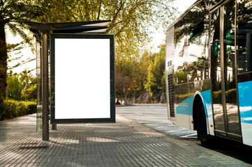 White blank vertical billboard at the bus stop on the city street. In the background of buses and...