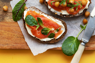 Breakfast starts a brisk day. Sandwich with slightly salted salmon, chickpeas and seasonal herbs. Healthy eating concept. On the tray is a snack and a knife with butter, a bright yellow background