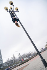 Young attractive Girl hanging by feet upside down on the street light in the street. super extreem. concept of courage and meditation