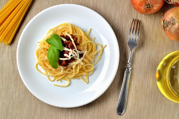 Italian traditional pasta meal. Spaghetti bolognese with cheese and basil. Onion, oil and fork in background. Top view.