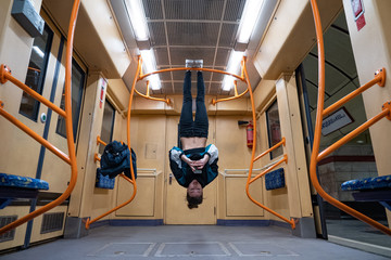 Girl hanging by feet upside down in the subway carriage and using smartphone. Concept of overusing...