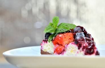 Delicious fruit strawberry and blueberry cream cake glazed by cherry sauce and fresh mint leaves on decorative white plate. Low depth of field.