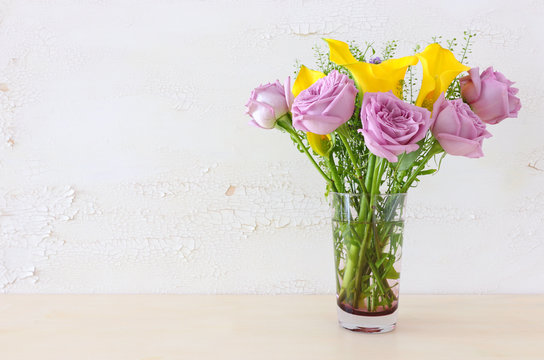 summer bouquet of pink roses and yellow calla lily flowers in the vase over wooden table and white old background