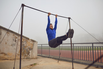 A bearded guy doing pull-ups on a horizontal bar in a stadium in the fog.