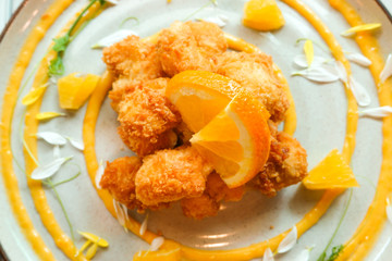 Crispy chicken nuggets golden deep fried with orange fruit, flower petals, vegetable and citrus dressing sauce delicious lunch meal food decorated on beautiful ceramic plate top view in restaurant