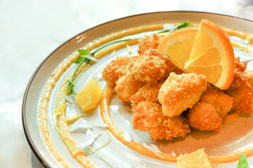 Crunchy chicken golden deep fried with orange fruit, citrus dressing sauce and floral petals decorated art hot served on Japanese plate delicious appetizer food meal side view in modern restaurant