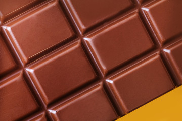 A bar of milk chocolate closeup on a yellow background. The concept of sweets, junk food. Detailed texture macro photo in warm colors.