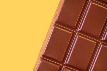 A bar of milk chocolate closeup on a yellow background. The concept of sweets, junk food. Detailed texture macro photo in warm colors.