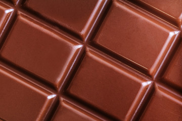 A bar of milk chocolate closeup. The concept of sweets, junk food. Detailed texture macro photo in warm colors.