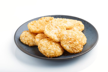 Traditional japanese rice chips cookies with honey and soy sauce on a blue ceramic plate isolated on white background. side view.
