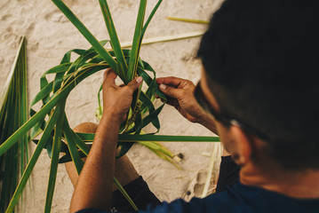 A man weaving a hat with palm leaves