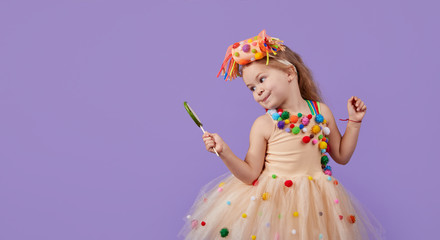 Childrens birthday party, masquerade. Little happy toddler child girl in a puffy tutu fancy dress, having fun on Violet background. Space for text