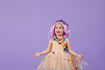 Childrens birthday party, masquerade. Little happy toddler child girl in a puffy tutu fancy dress, having fun on Violet background. Space for text