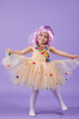 Childrens birthday party, masquerade. Little happy toddler child girl in a puffy tutu fancy dress, having fun on Violet background. Space for text
