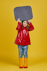 Little child girl holding black chalkboard banner on yellow background. Funny Face. Copy space for text. Advertising seasonal childrens products