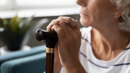 Close up of sad lonely old lady with walking stick lost in thoughts thinking and pondering at home, upset abandoned middle-aged 60s woman with cane feel distressed, elderly solitude concept