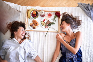 top view of lesbians laughing, holding hands, lying on bed. lesbian, couple, romance concept