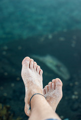 Fototapeta na wymiar Bare feet of a girl with sand on a background of green sea water