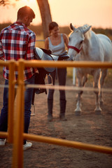   man and woman with horse at  ranch.Man prepare saddle for  horse.