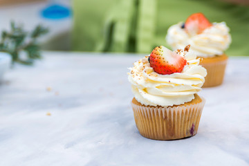 Tasty cream cheese cupcakes. Woman cooking cakes. Confectioner decorating cupcakes with strawberry. Cooking class, culinary and bakery. Fruit cupcakes on table.