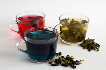 butterfly Blue hot tea. Three glass cups with blue, red and green tea with dry tea leaves and flowers on a white background. Red hot Hibiscus tea. Green hot tea. Hot drinks. Healthy lifestyle.