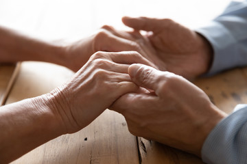 Crop close up of mature old husband and wife hold hands show love and care, middle-aged 60s couple spouses having close tender romantic moment at home, elderly relationships, marriage concept