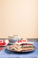 Homemade layered cake with pomegranate jam and a cup of coffee on a black black and orange background. side view, selective focus.
