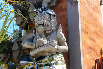 A close up on a guardian figure next to a Hindu temple on Bali, Indonesia. The figure is wrapped in checked material tied with yellow ribbon. Tradition and history.