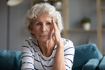 Upset depressed elderly woman sit on couch look in window distance pondering having problems,...