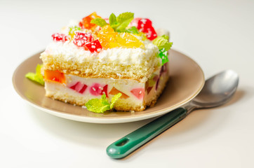 Obraz na płótnie Canvas A portion of cream cake with pieces of colorful jelly and sprinkled with coconut flakes