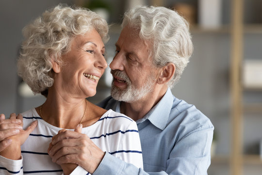 Smiling mature 60s couple spouses embrace look in eyes show love and affection, happy middle-aged old husband and wife hug and cuddle share romantic tender moment together, elderly marriage concept