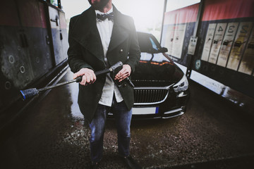 Plakat Hands of an adult and elegant looking male holding a water jet in front of the car in a carwashing station